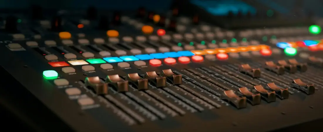 Close-up of a professional sound mixer with colorful glowing controls in a dimly lit studio.